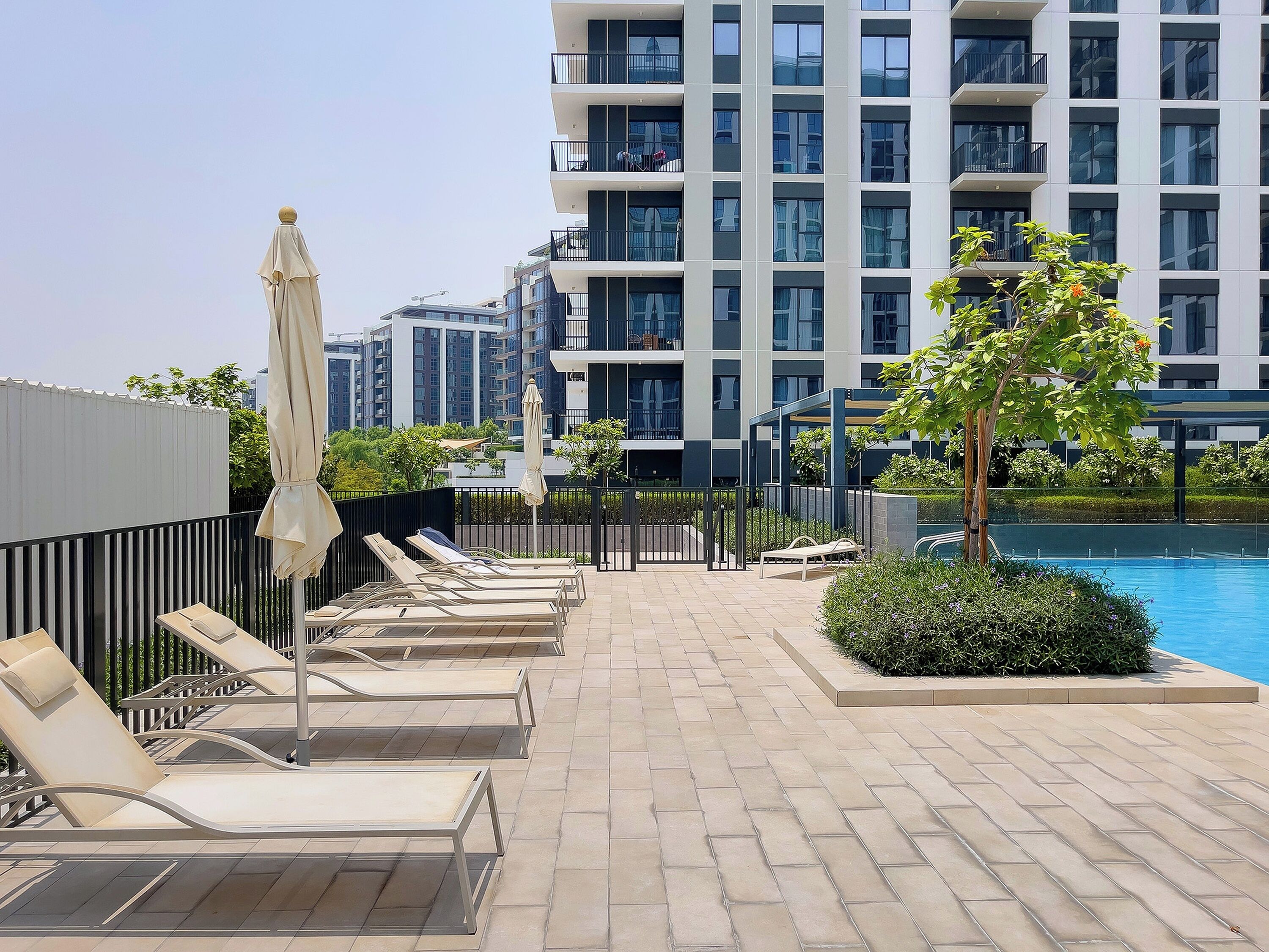 Un espace piscine aménagé sur le toit, avec des chaises longues et des parasols, entouré d’un immeuble de grande hauteur doté de balcons.