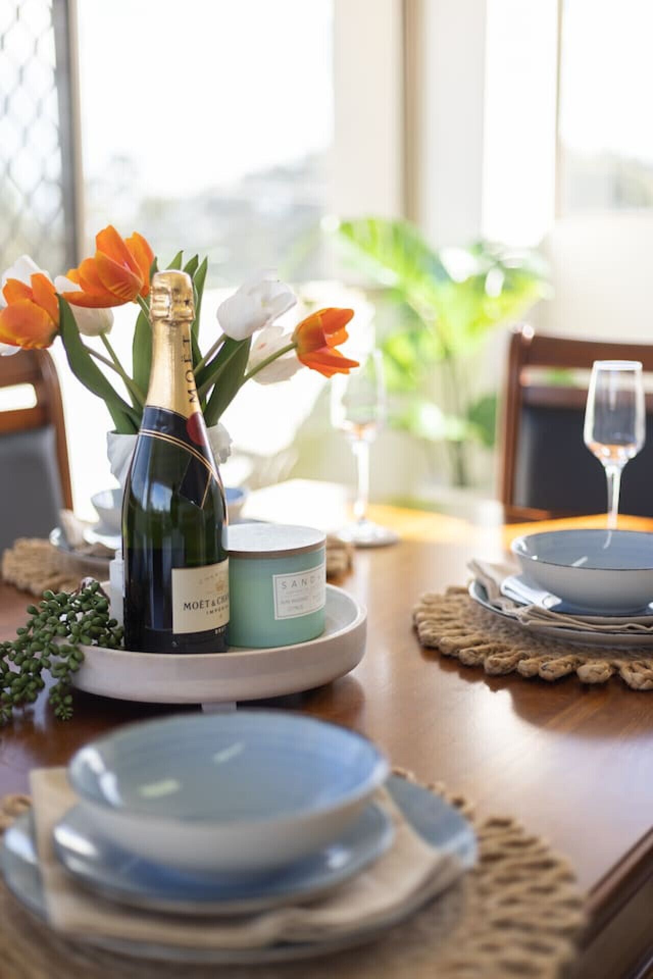 Ein Esstisch ist gedeckt mit Tellern, einer Flasche Moët & Chandon Champagner, einer Kerze und Tulpen.