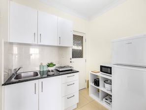 Una cocina con armarios blancos, un fregadero, un microondas y un refrigerador.