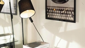 A glass table with a lamp and books, a framed picture on the wall, and a window reflecting the room. - Lovely tiny home at Sunnybank CBD Street Parking (Sunnybank)