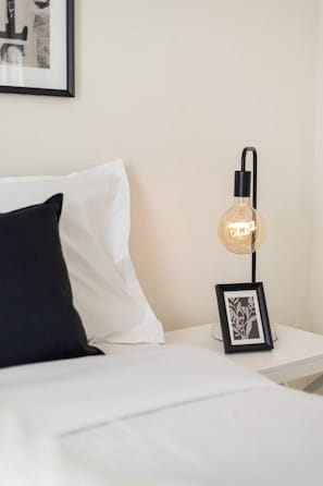 Un dormitorio con cama, mesita de noche, cuadro enmarcado y lámpara de pared.