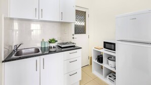 A modern kitchen with white cabinets, a black countertop, and a white refrigerator. - Lovely tiny home at Sunnybank CBD Street Parking (Sunnybank)