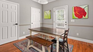 Un espace repas comprenant une table et un banc en bois, deux portes et deux œuvres d’art encadrées accrochées aux murs.