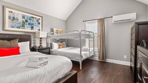 Une chambre d’hôtel avec un lit superposé, un bureau avec une lampe, une commode et un appareil de climatisation.