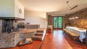 A spacious room with a fireplace, a dog bed, a long dining table, and a stone wall. - I Tre Castagni by Interhome (Piegaro)