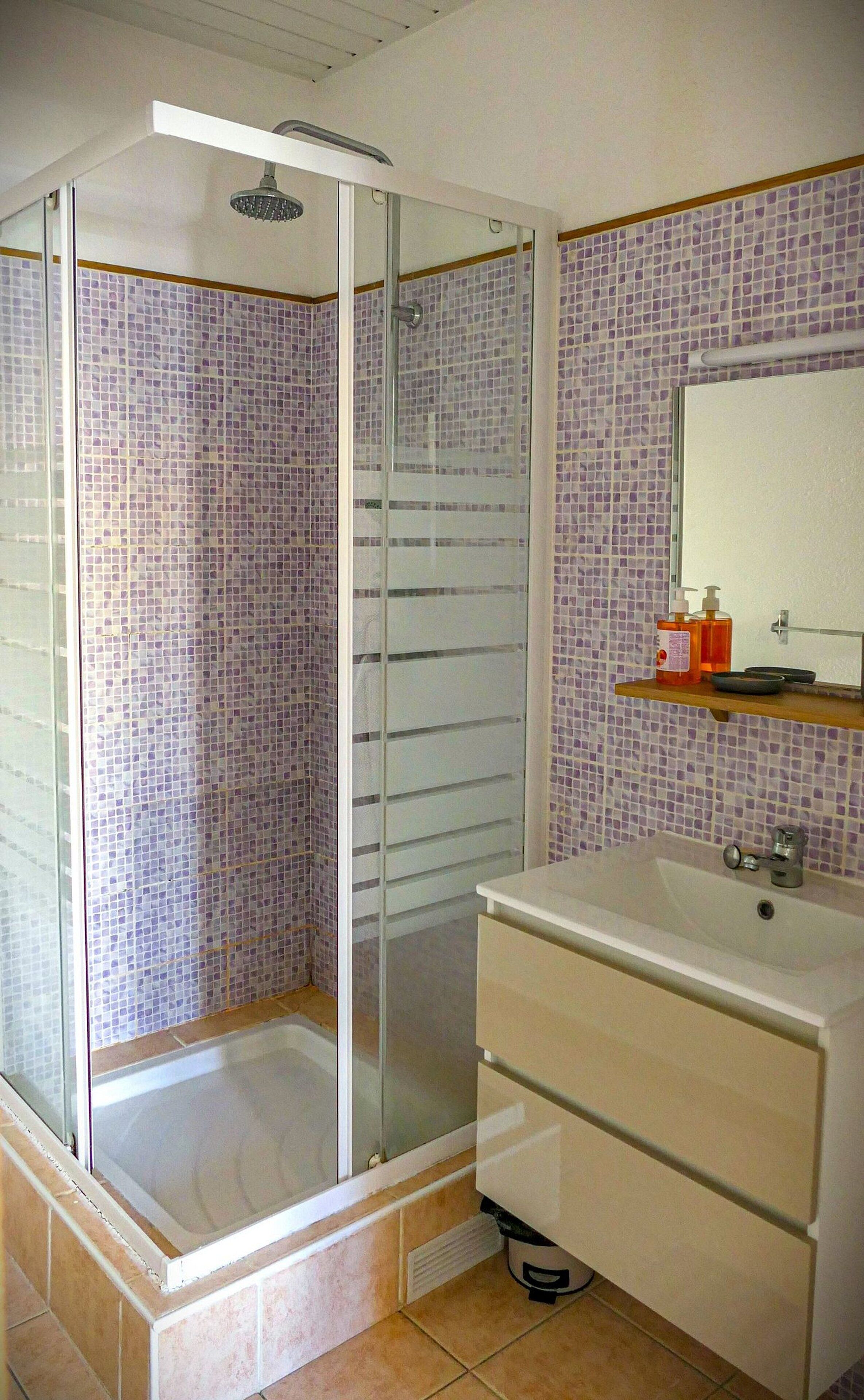 Un baño con cabina de ducha de vidrio, lavamanos con espejo y salpicadero de azulejos.