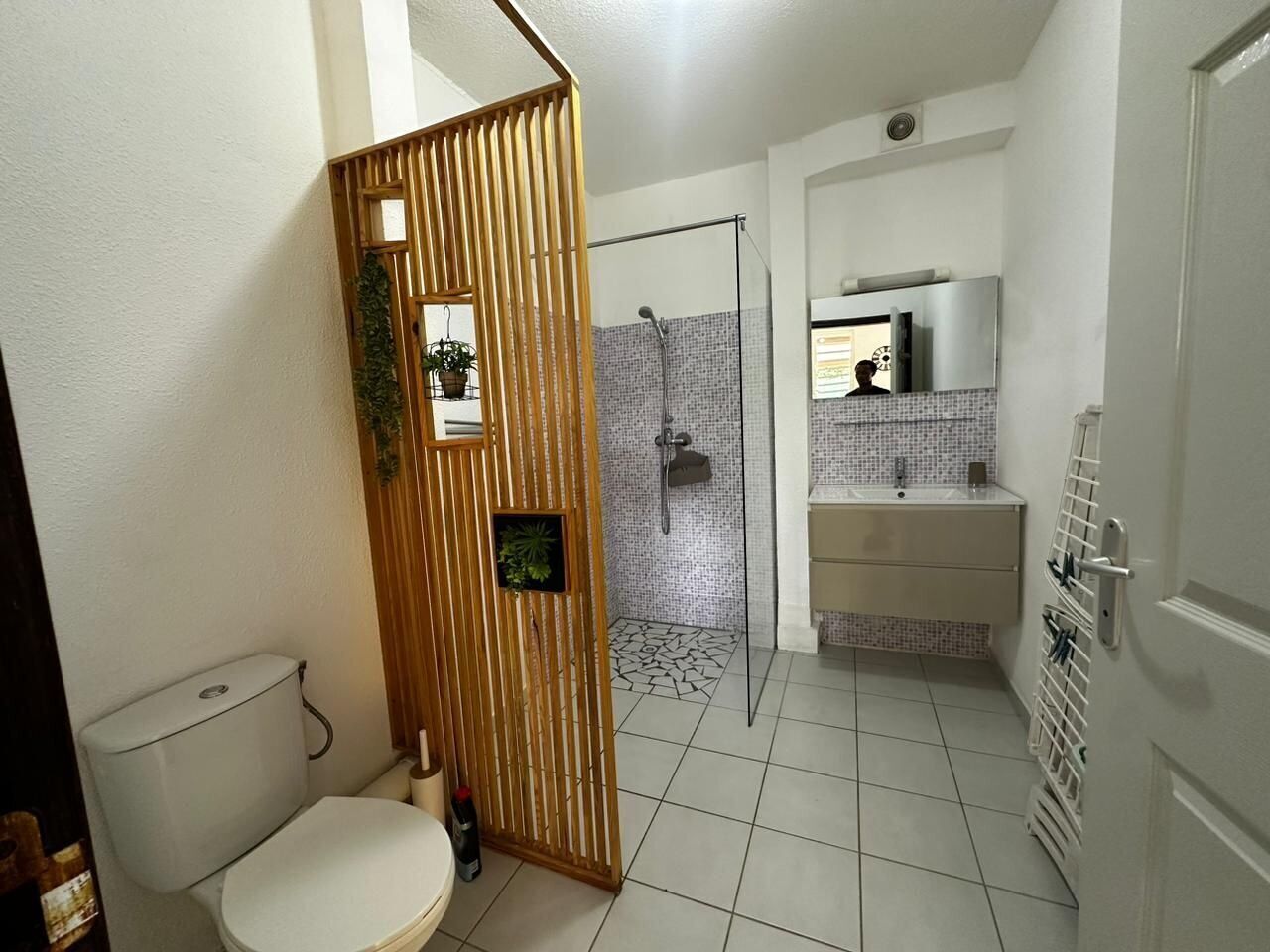Een badkamer met toilet, douche, wastafel en een houten scheidingswand.
