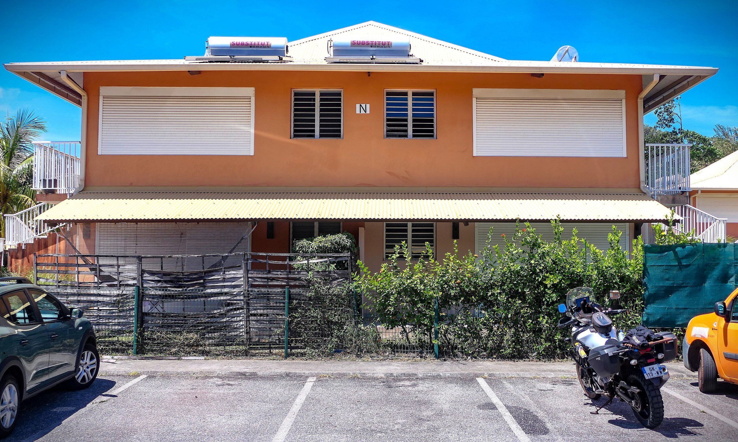 A two-story building with a yellow facade, a covered entrance, and a gated parking area.