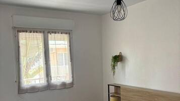 A bedroom with a bed, a hanging plant, and a window with curtains.