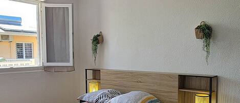 Une chambre à coucher avec un lit, deux tables de chevet, un luminaire suspendu, une fenêtre et une vue sur l’extérieur.
