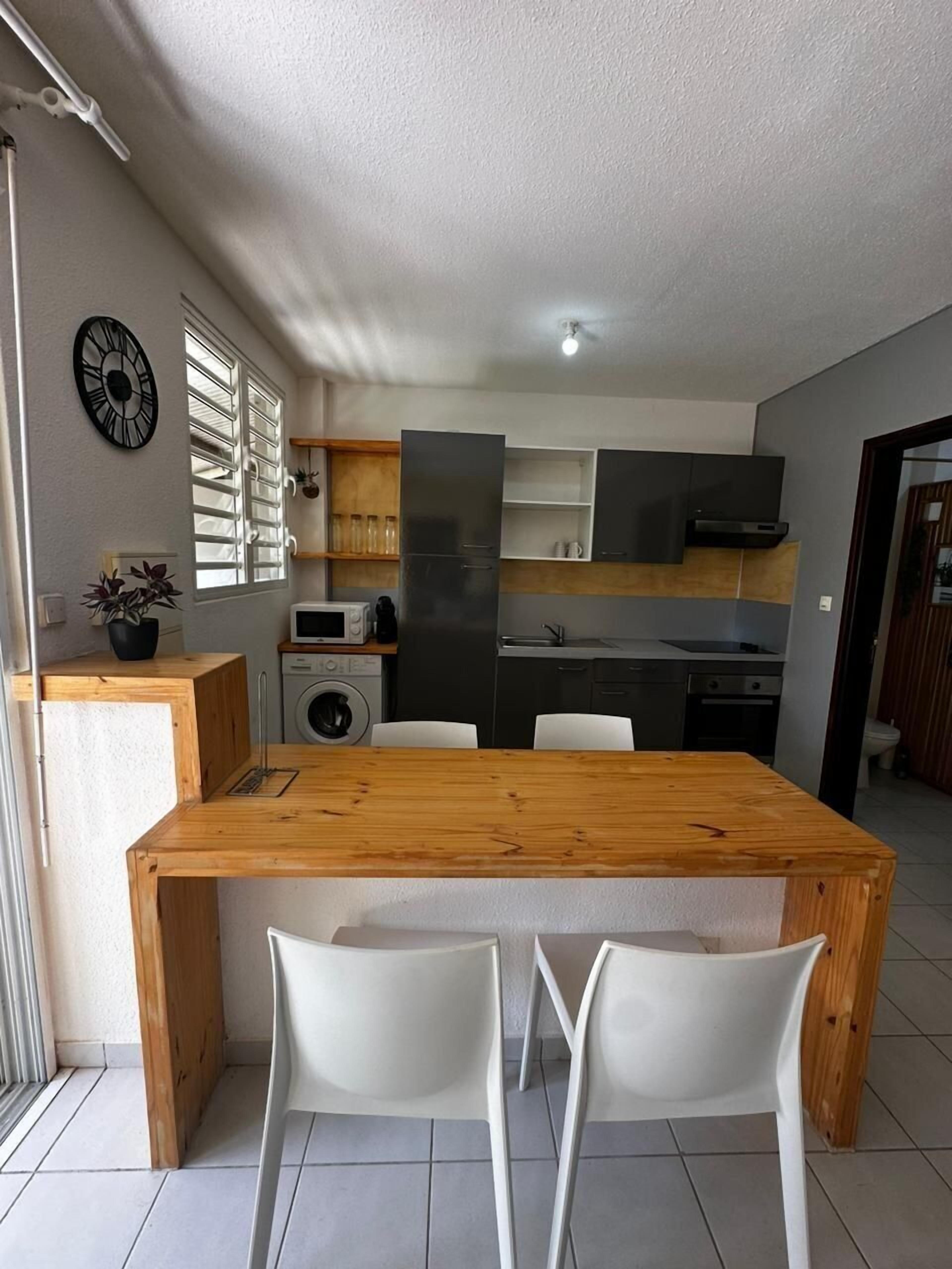 Una cucina compatta con un tavolo da pranzo in legno e sedie bianche, una lavatrice e un forno a microonde.