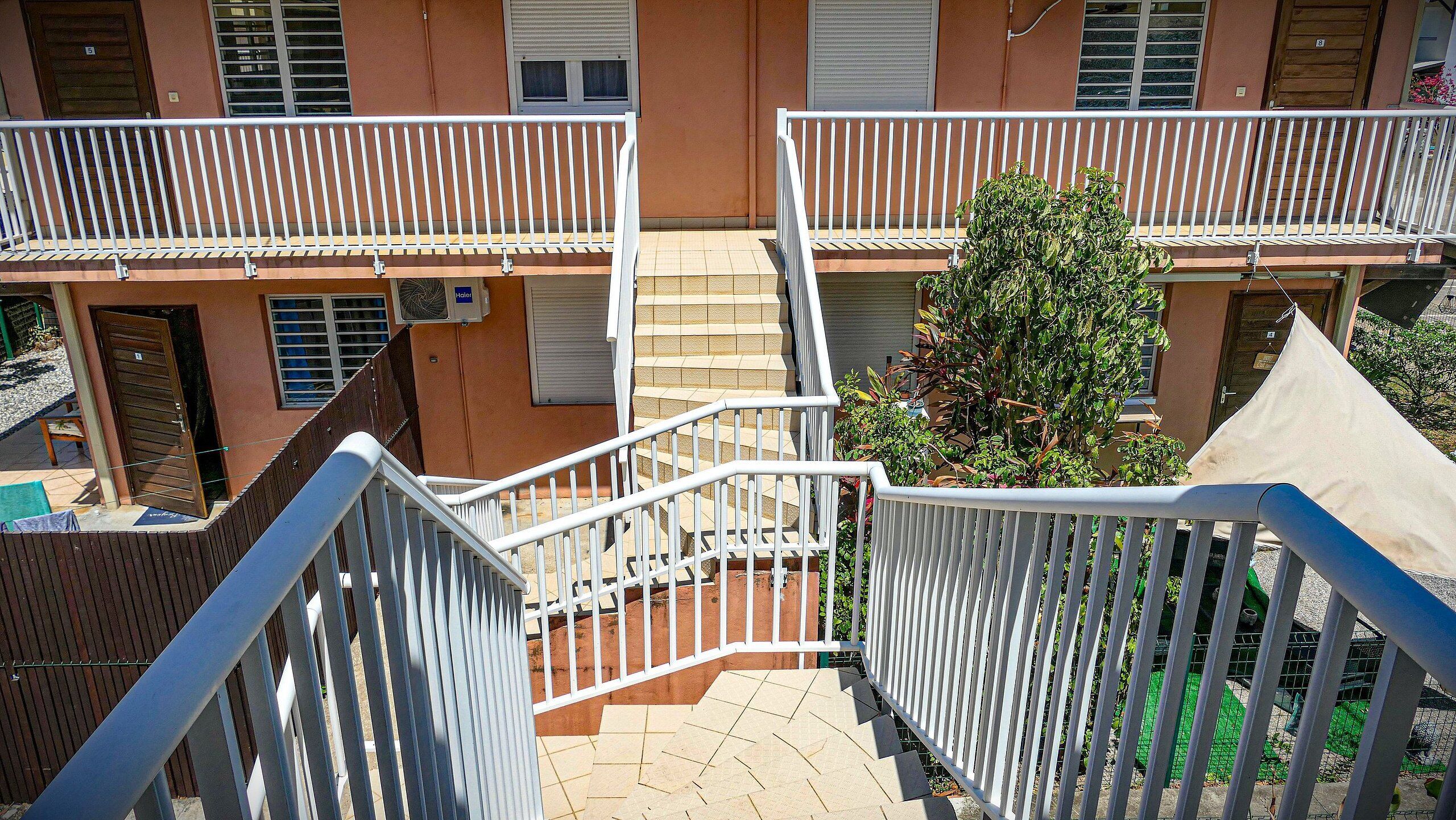 A multi-level residential building with balconies, a staircase, and a small garden area.