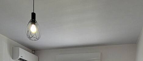 A bedroom with a bed, a window, an air conditioner, and a lamp.