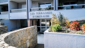 A building with a sign reading "LES TERRASSES D'EMERAUDE". It features a stone wall, a small garden with plants, and a modern architectural style with balconies. - Terrasses d'Emeraude by Interhome (Dinard)
