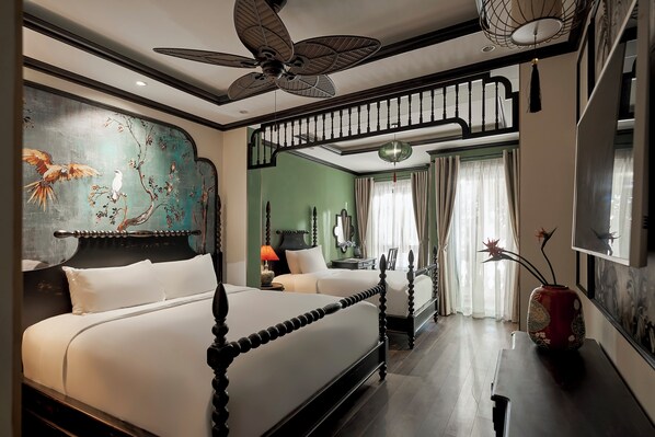 A bedroom with a large bed, a smaller bed, a ceiling fan, a nightstand, a vase, and a painting on the wall.
