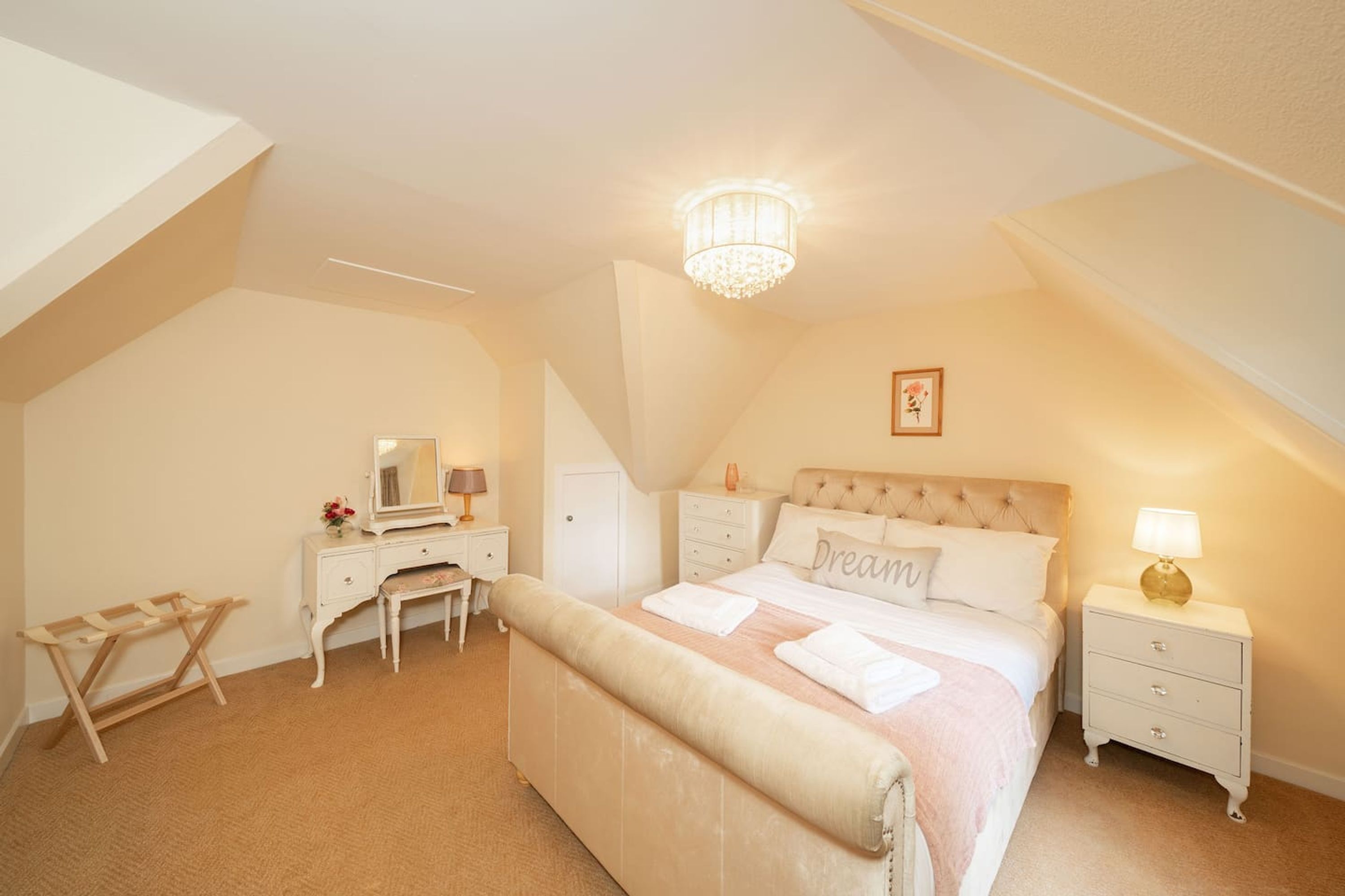 A bedroom with a large bed, a nightstand, a dresser, a vanity, and a chandelier.