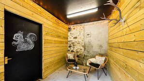 Una habitación acogedora con paredes de madera, una puerta negra con un diseño de ardilla blanca, dos sillas de mimbre, una mesita con tazas y una decoración de corno de ciervo.