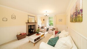 Un salón acogedor con chimenea, muebles blancos y un ventanal grande.