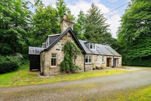 Une petite maison en pierre avec un toit à pignon, une cheminée et un petit porche.