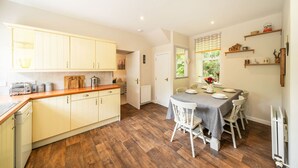 Una cocina amplia con suelo de madera, un comedor con mesa y sillas, y una ventana con vistas a zonas verdes.