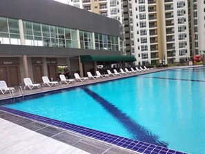 Una piscina con sillas de descanso y un edificio de varios pisos al fondo.