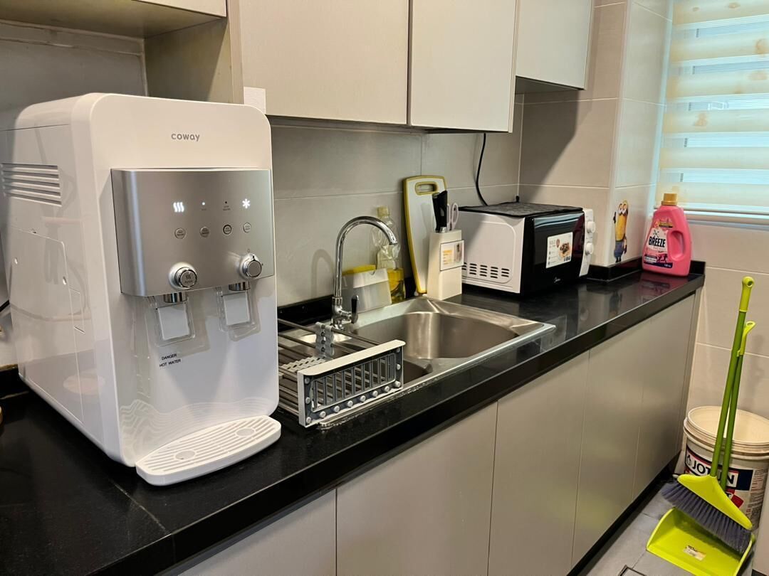 A kitchen with a water dispenser, a toaster, a sink, and a window with blinds.