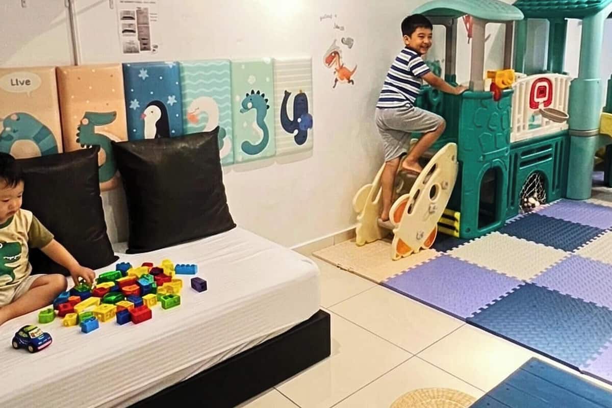 Een kind speelt met bouwstenen op een bed, een speelruimte met een glijbaan, en educatieve wanddecoraties.