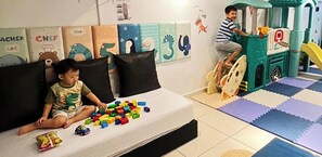 Niño jugando con bloques de construcción en una cama, zona de juegos con un tobogán y decoraciones educativas en la pared.