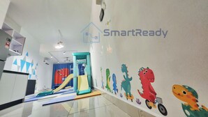 Zona de juegos infantiles con un tobogán, pared de escalar y una pared decorada con personajes de dibujos animados.