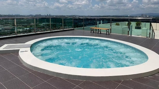 Una piscina en la azotea con un banco, rodeada por una baranda de cristal, con vistas a un paisaje urbano.