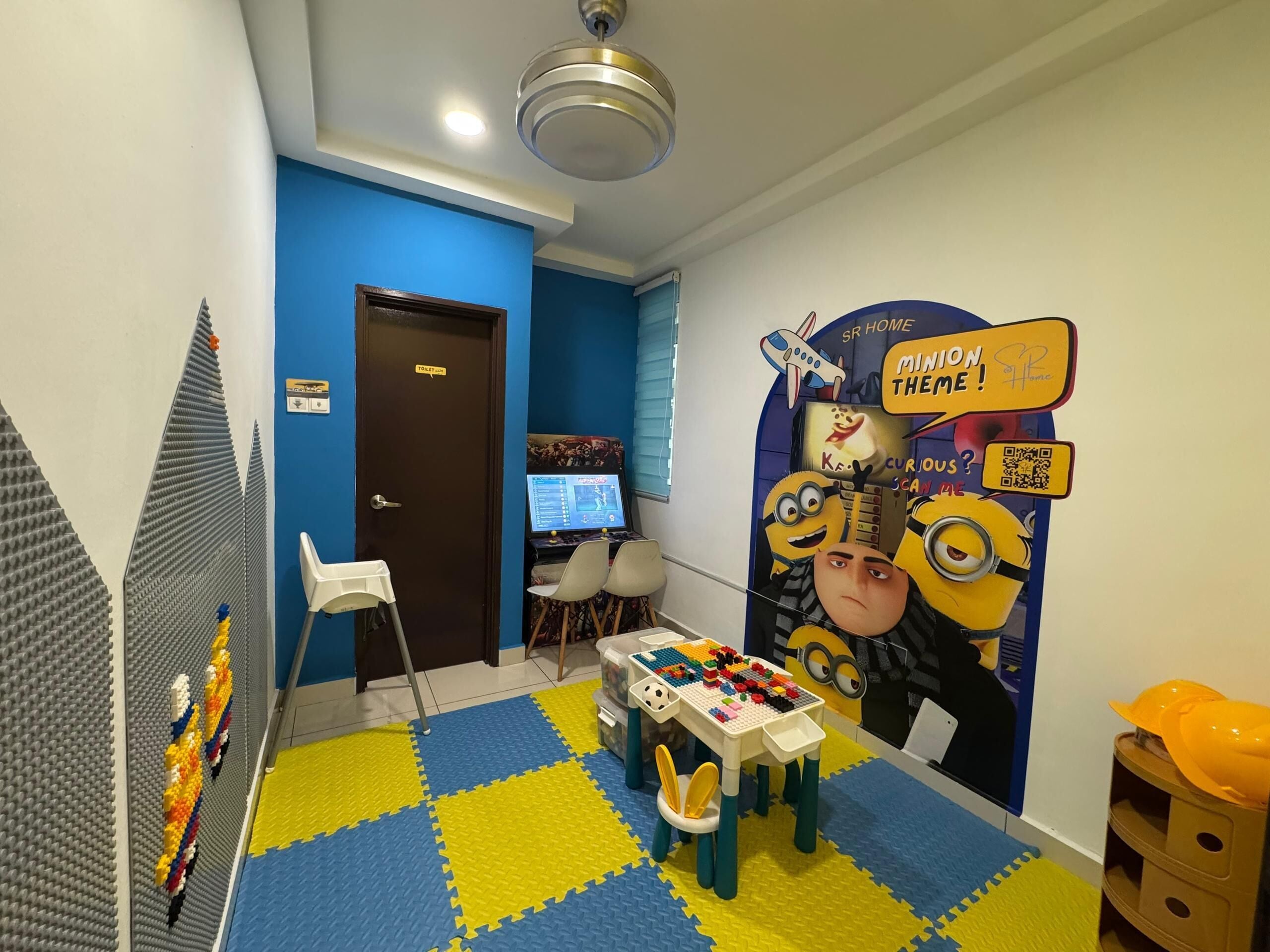 A children's play area with a Minion-themed backdrop, a play table with building blocks, and a computer setup.