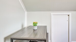 Una pequeña mesa rectangular con un jarrón blanco lleno de flores, ubicada frente a una pared blanca con una puerta a la derecha.