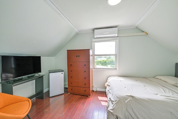 Un dormitorio con cama, cómoda, escritorio y televisión, y una ventana.