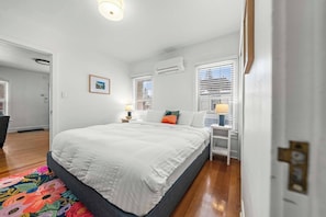 Un dormitorio con cama, mesita de noche, lámpara y ventana con persianas.