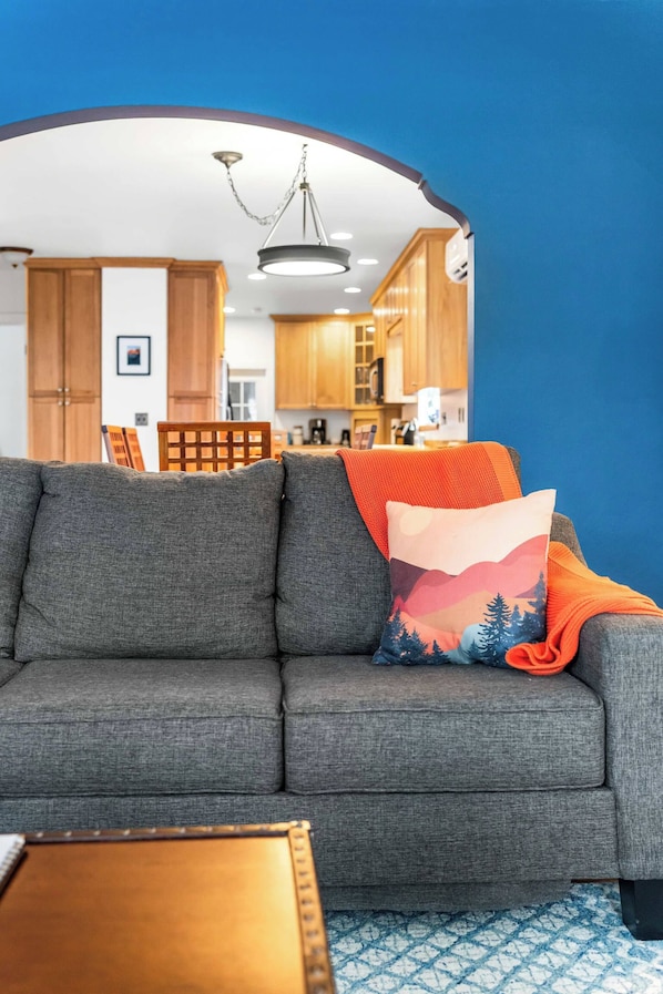 Una sala de estar con un sofá gris, una mesa de centro de madera y una alfombra azul estampada.