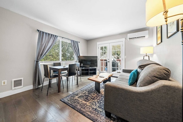 A living room with a sofa, a coffee table, a TV, and a dining area with chairs and a table.