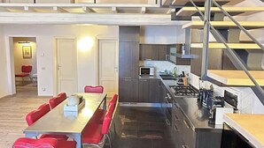 Una cucina moderna con isola centrale, zona pranzo con sedie rosse e una scala che conduce a un piano superiore.