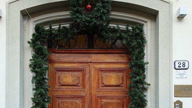 Una porta in legno doppia con un'corona natalizia e una ghirlanda, una cassetta delle lettere e il numero civico 28.