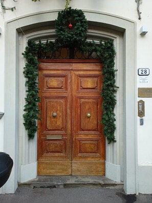 Een houten dubbele deur met een kerstkrans en guirlande, een brievenbus en huisnummer 28.