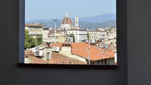 Una stanza con un'ampia finestra che si affaccia su un panorama urbano, caratterizzato da una cupola imponente e diversi edifici.