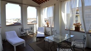 Un balcone luminoso con un letto, sedie e un tavolo, che offre vista sulla città.