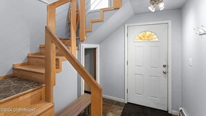 A staircase with wooden railings leading to a landing, a white door with a decorative glass panel, and a ceiling light fixture. - "Bright and Stylish Anchorage 2 - Bedroom House - "7 mins from ANC" (Anchorage)