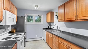 A kitchen with wooden cabinets, a white stove, a black countertop, and a window with a view of trees. - "Bright and Stylish Anchorage 2 - Bedroom House - "7 mins from ANC" (Anchorage)
