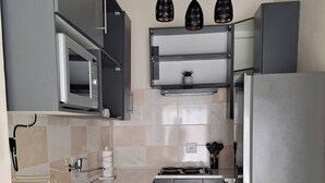 Una cocina moderna con armarios grises, un refrigerador de acero inoxidable, un microondas, un lavamanos y una lavadora.