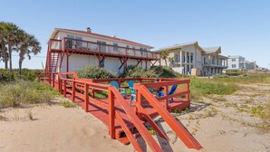 Ein Strandgrundstück mit roter Holzterrasse, einem Pool und einem großen Haus mit mehreren Balkonen.