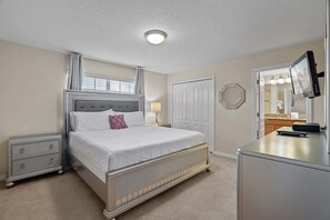A bedroom with a bed, nightstand, dresser, and a television on a stand.
