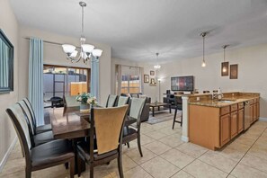 A spacious kitchen with a central island, dining area with chairs, and a TV mounted on the wall.