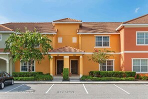A multi-story hotel with a consistent architectural style, featuring a central entrance with a covered porch, multiple windows, and a parking lot in front.
