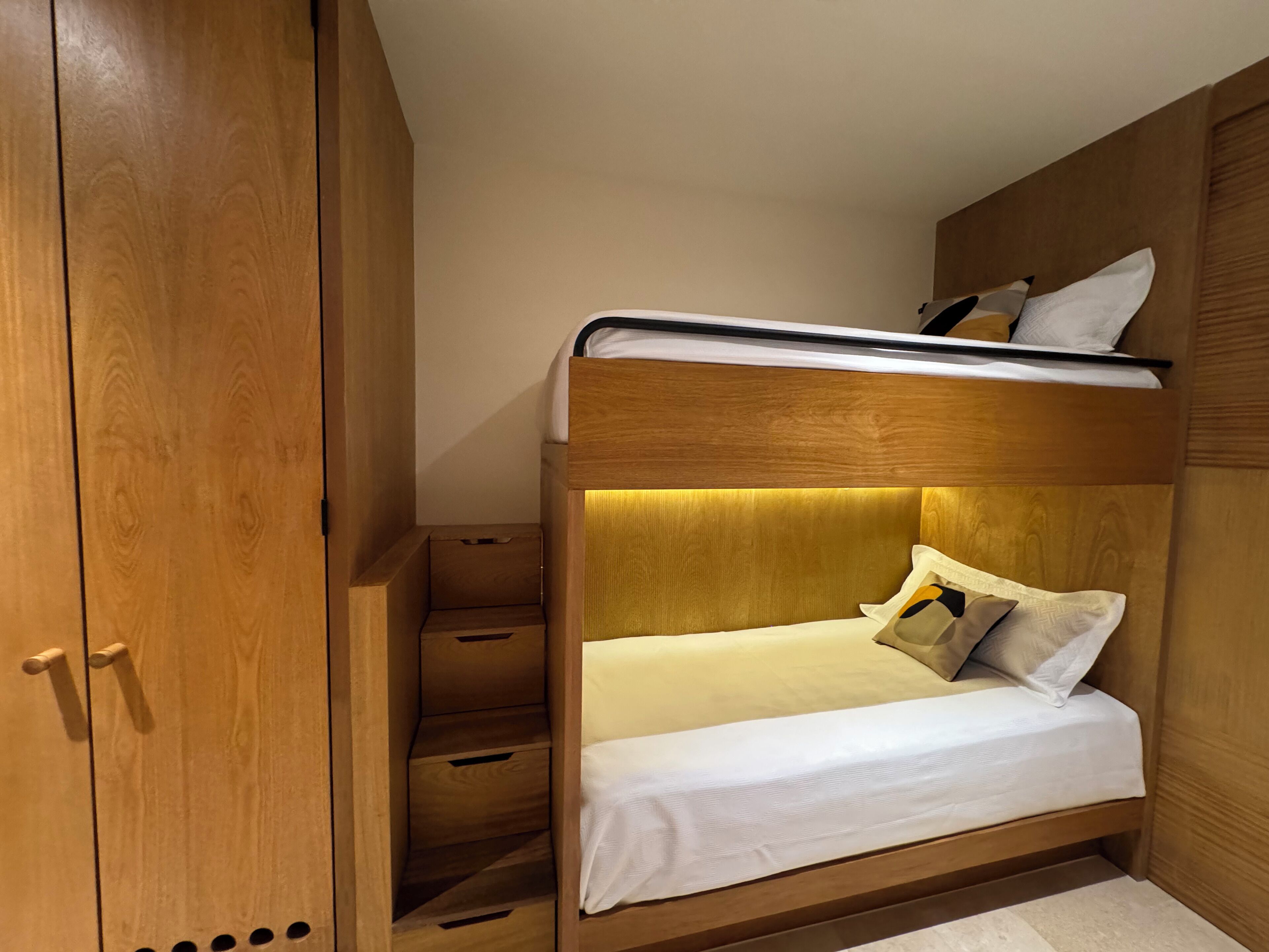 A compact bedroom with a bunk bed, wooden wardrobe, and built-in drawers.