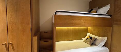A compact bedroom with a bunk bed, wooden wardrobe, and built-in drawers.